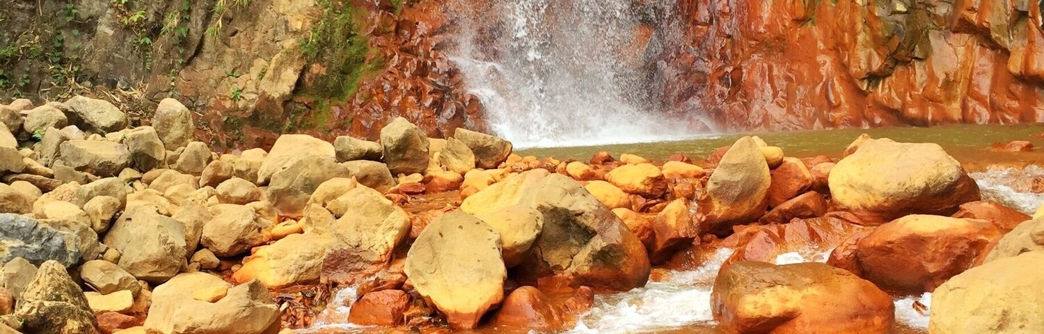 A waterfall cascading over reddish-brown rocks into a shallow stream with large boulders.