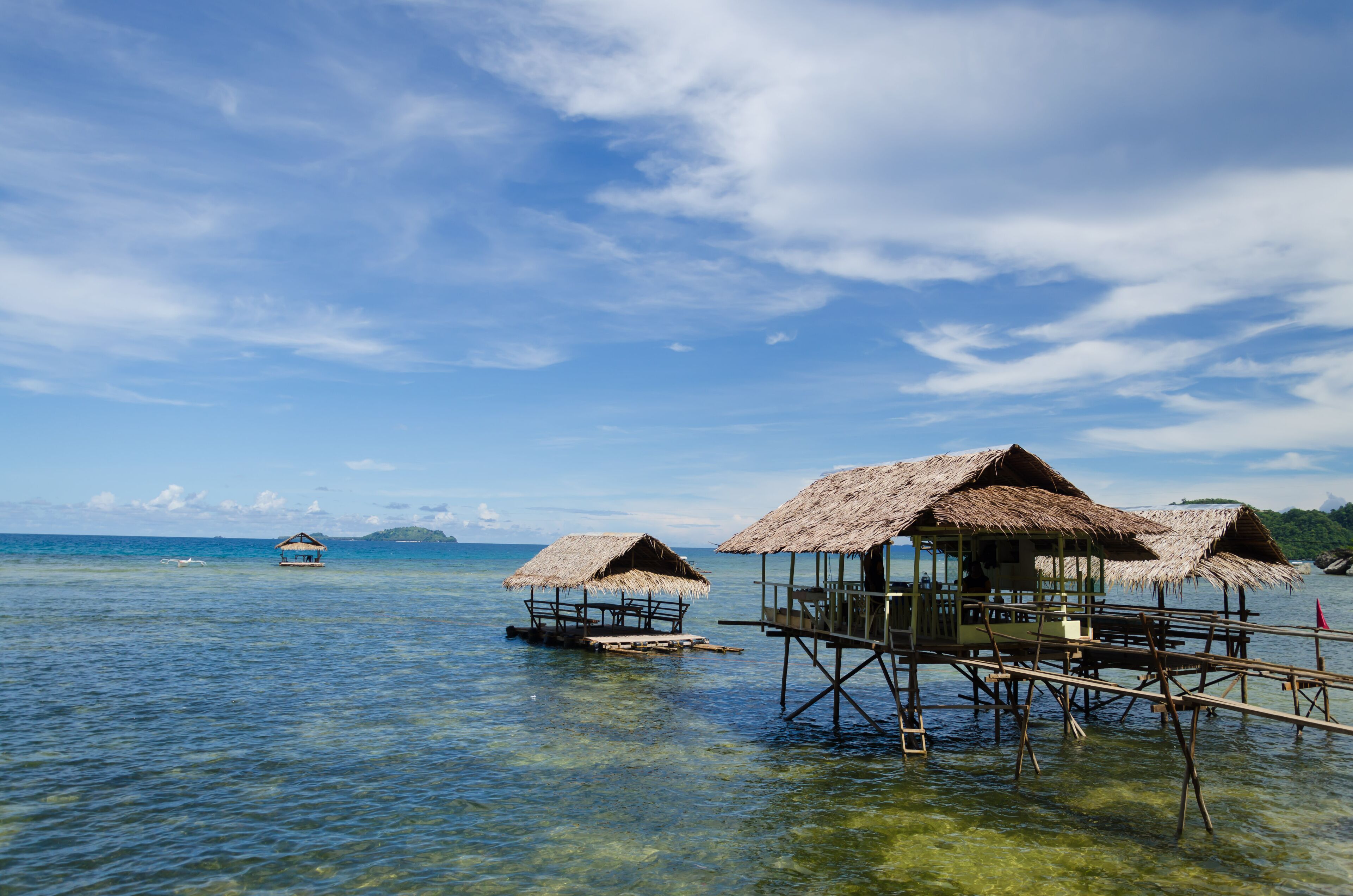 Overwater bungalows with thatched roofs on stilts in clear blue water.