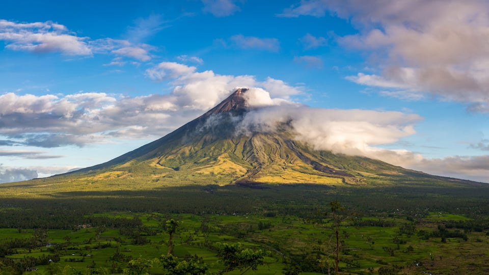 A volcano with a forested base and a clear sky.
