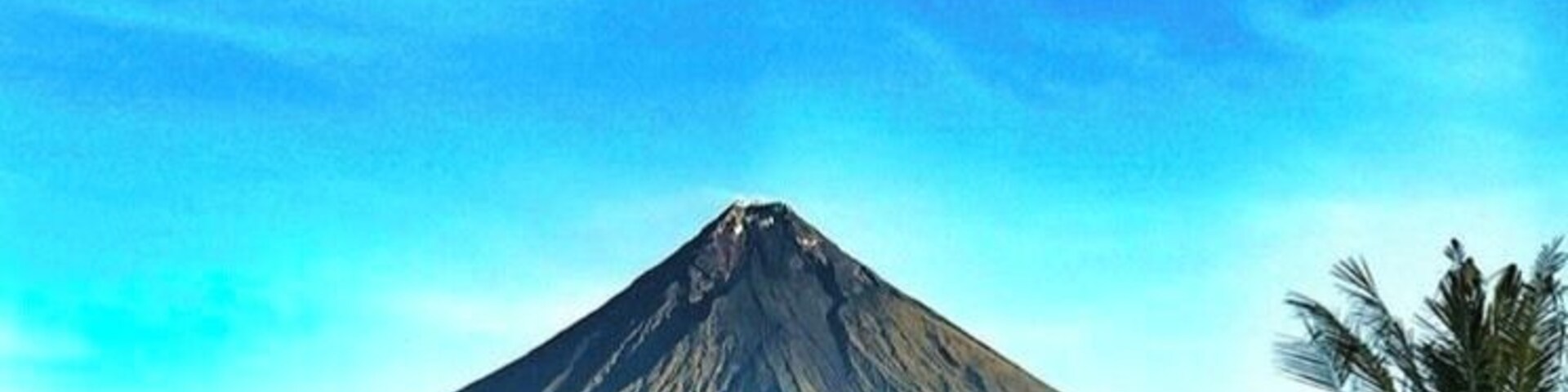 Una montaña de forma cónica, rodeada de palmeras.