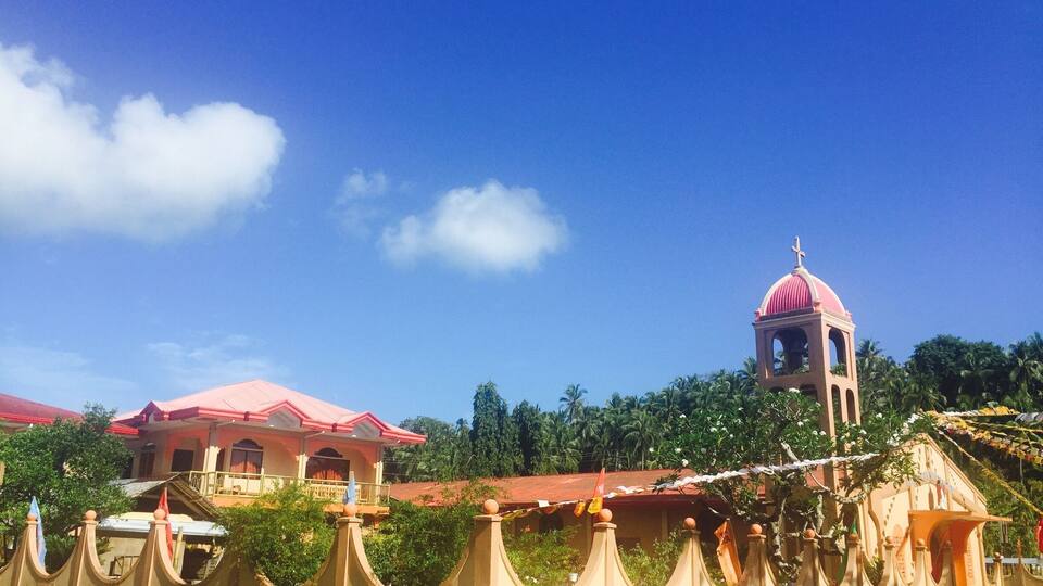 A church with a pink dome and bell tower, surrounded by a walled garden with palm trees.