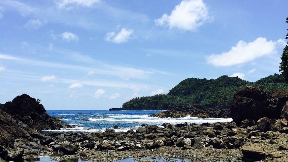 A rocky shoreline with clear blue water and a person swimming.