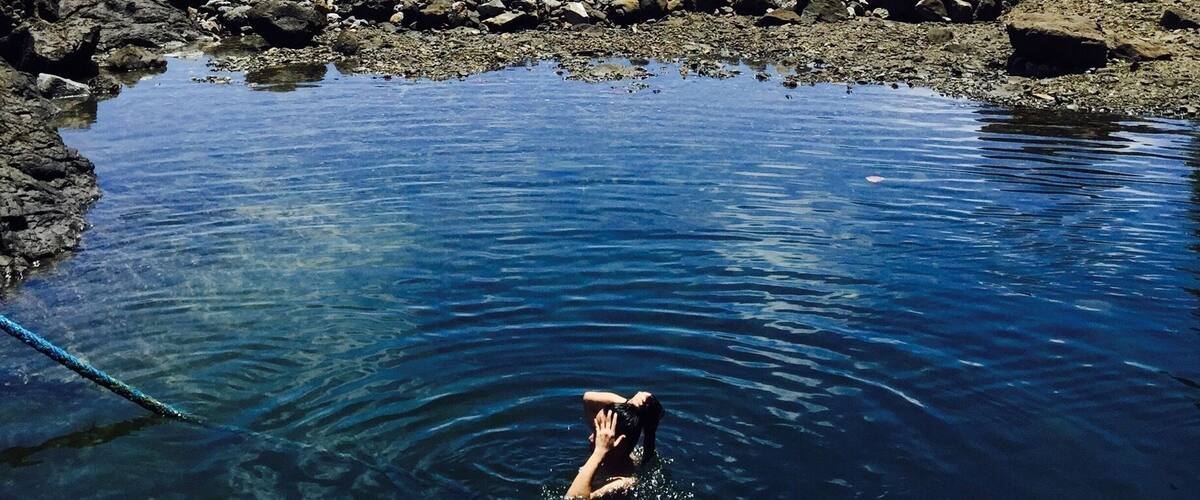 A rocky shoreline with clear blue water and a person swimming.