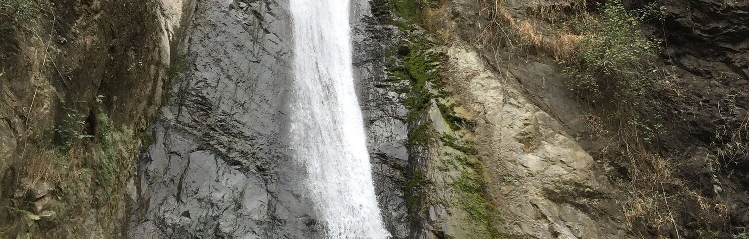 A waterfall cascading down a rocky cliff into a river surrounded by boulders and sparse vegetation.