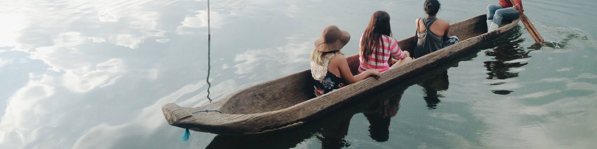 A group of people in a wooden boat on a calm lake with distant mountains.