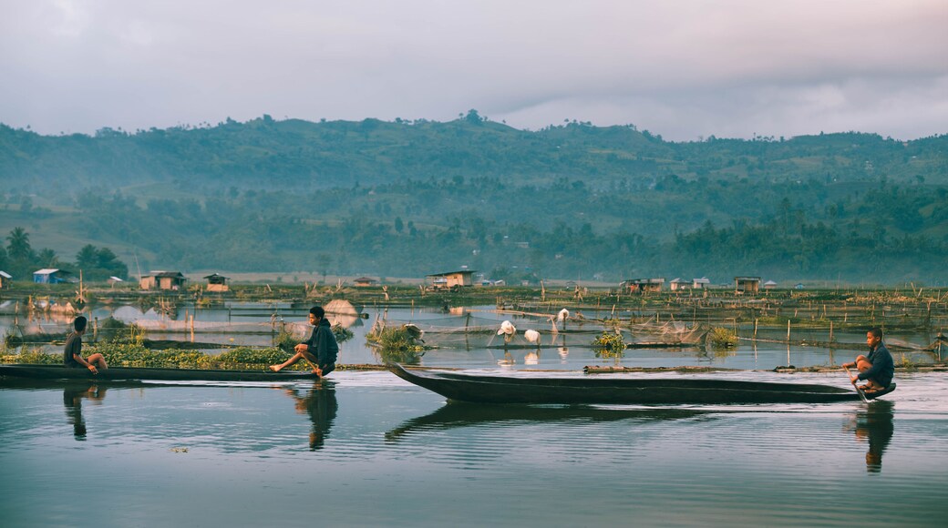 Lake Sebu, Philippines - 29 May 2015: View of tranquil waters reflecting the soft sky, with traditional boats carrying figures amidst the floating gardens and distant hills.