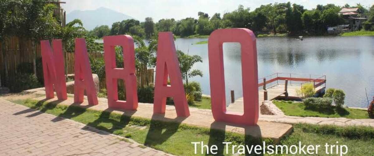 A sign with the letters 'NABAQ' in red, a lake, and a bridge in the background.