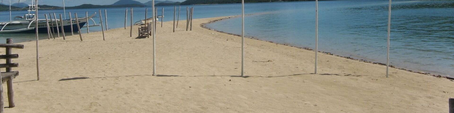 A sandy beach with flags, a boat, and a mountain in the background.