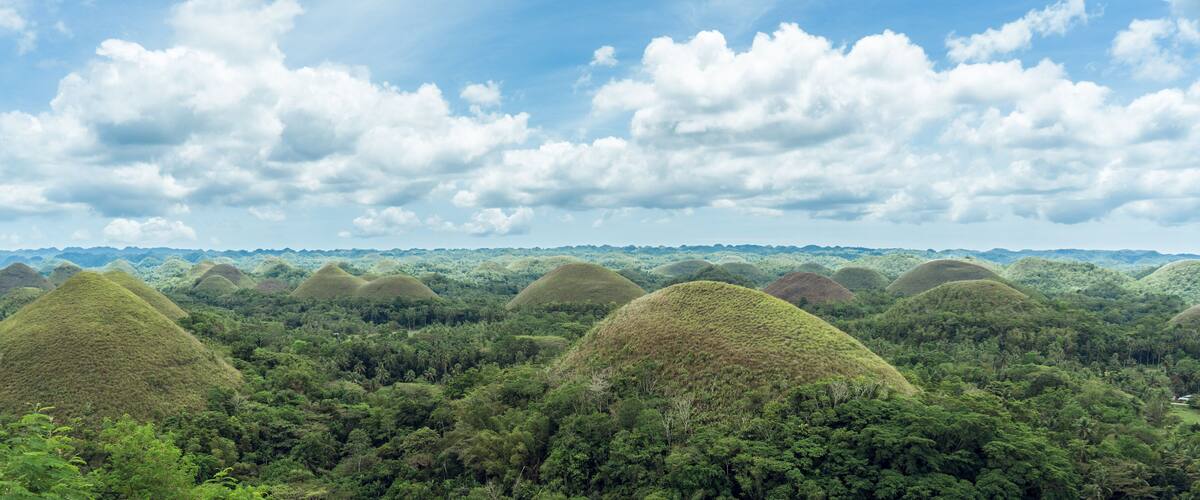 A landscape with numerous conical mounds surrounded by dense green forest under a partly cloudy sky.