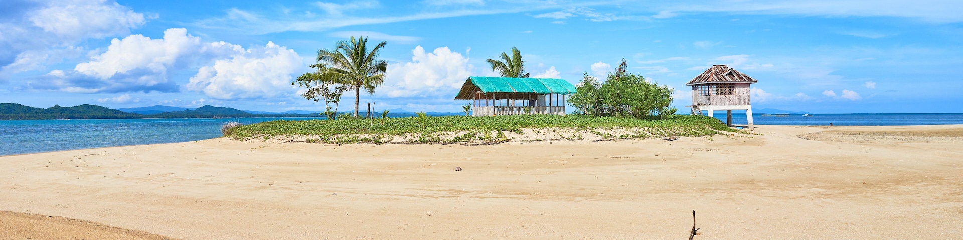 A beach with a blue boat, palm trees, and two small huts.