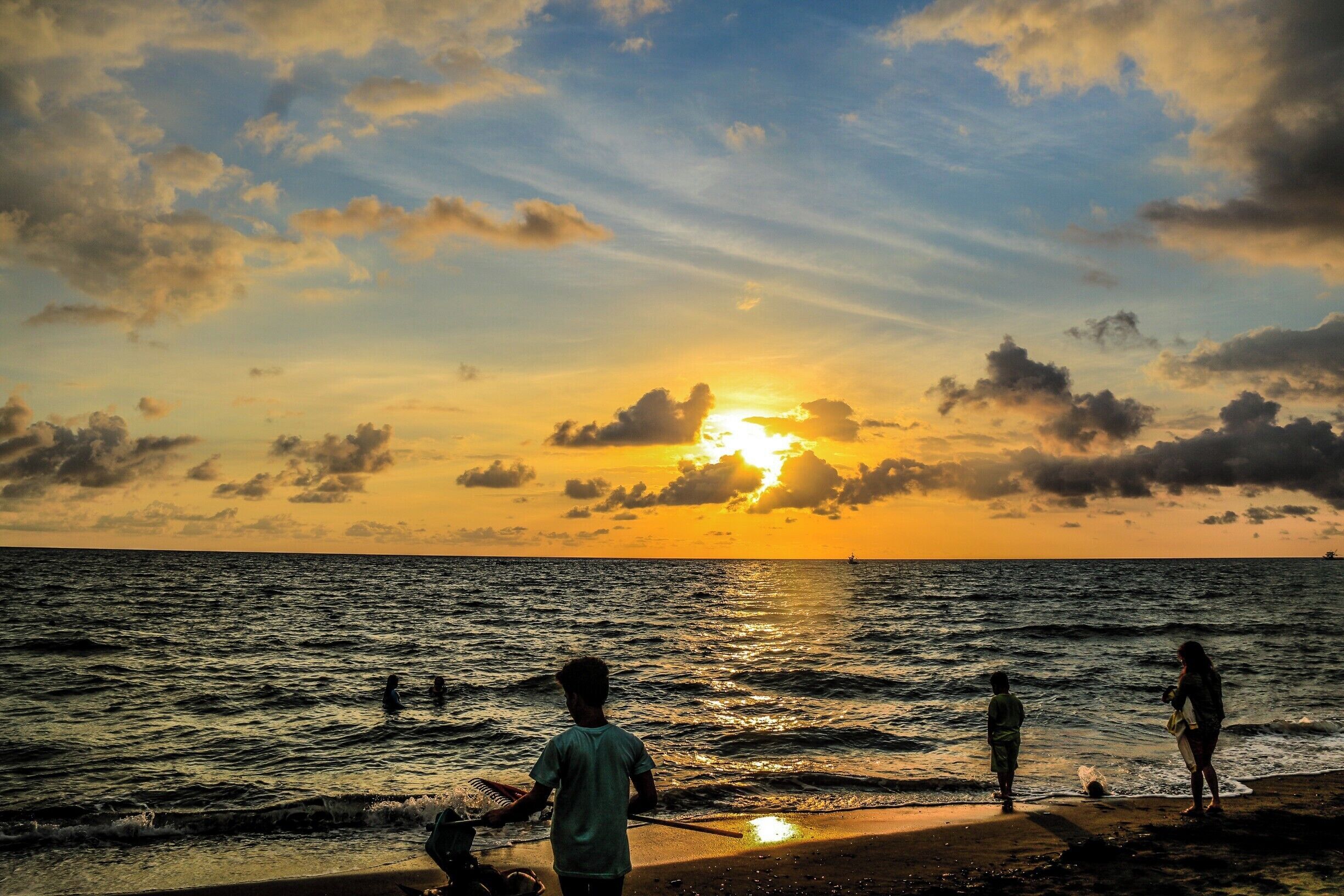 A sunset over the ocean with people standing on the shore.