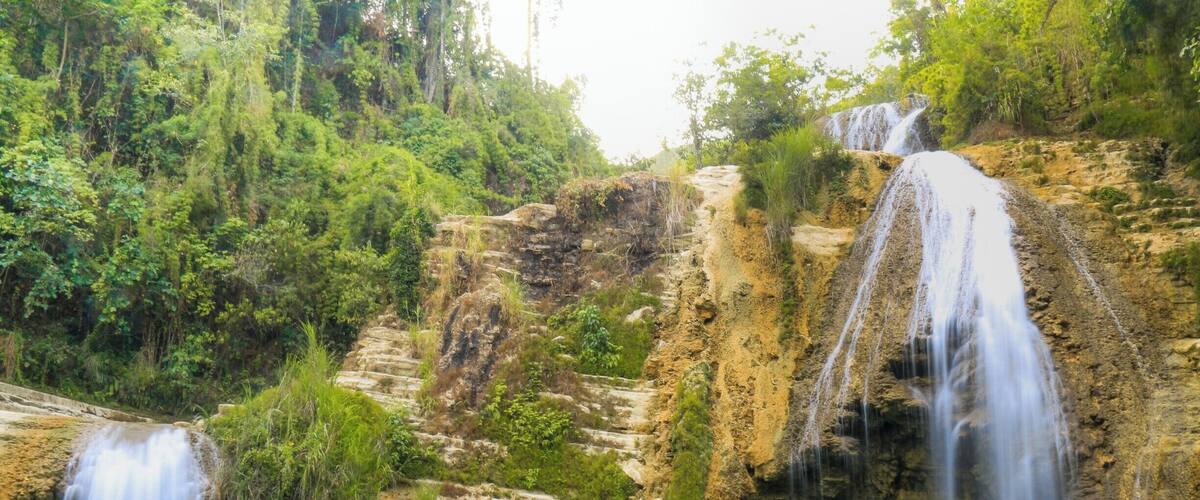 A waterfall cascading into a turquoise pool surrounded by lush greenery and rocky cliffs.