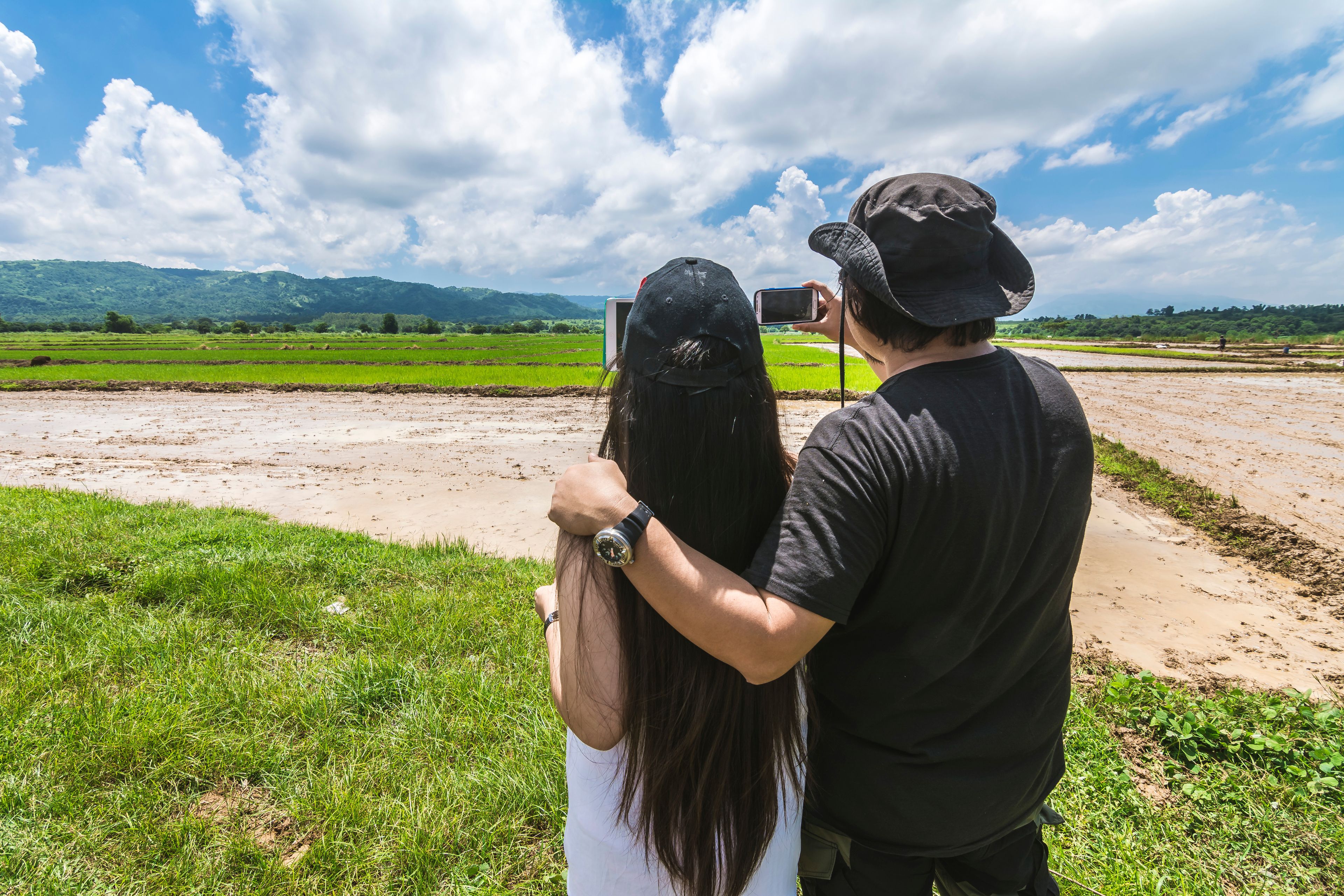 Two people embracing in a rural landscape with green fields and a mountain in the background.