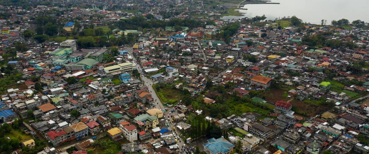 An aerial view of a coastal city with dense housing, a prominent church, and a large body of water.