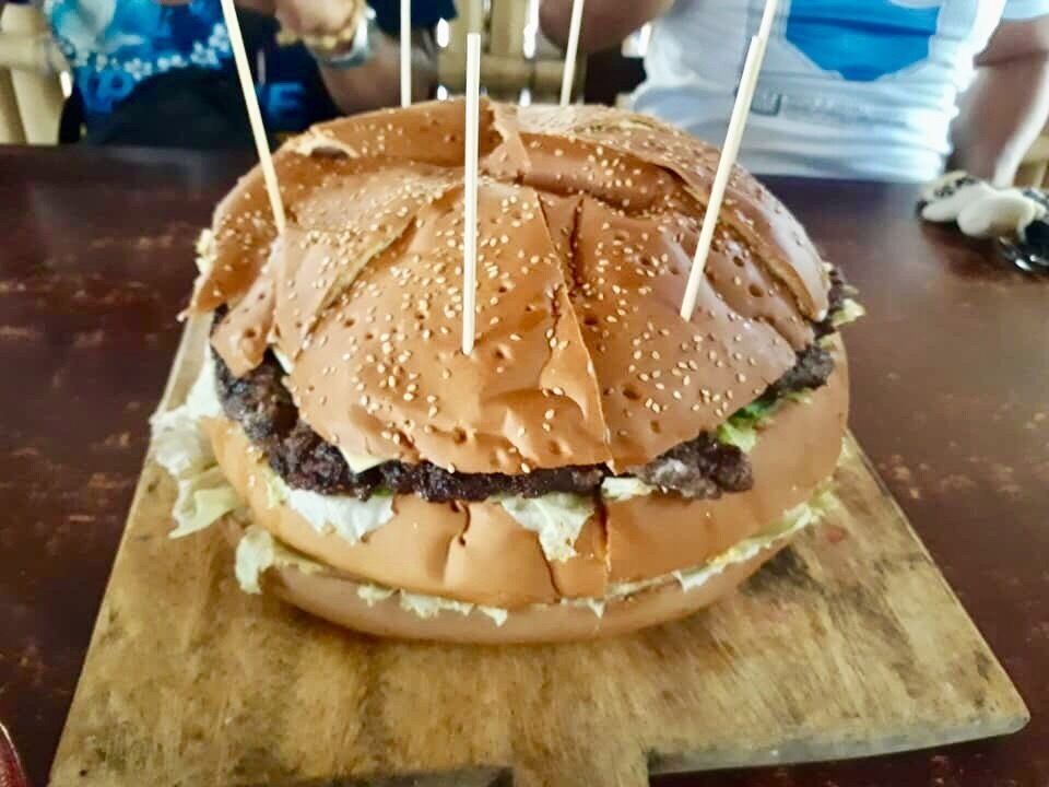 A burger with sesame seeds and toothpicks on a wooden board.