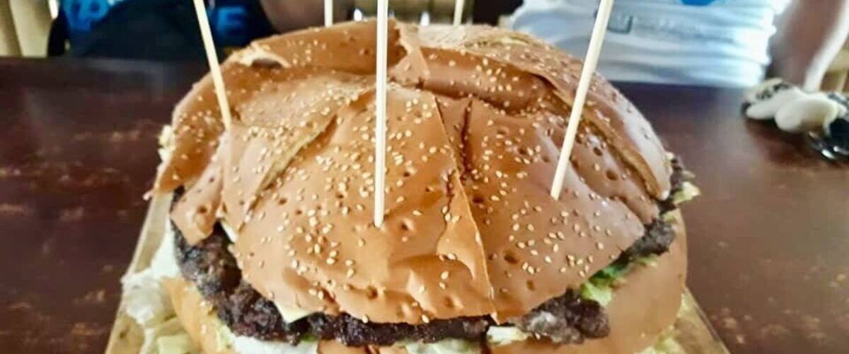 A burger with sesame seeds and toothpicks on a wooden board.