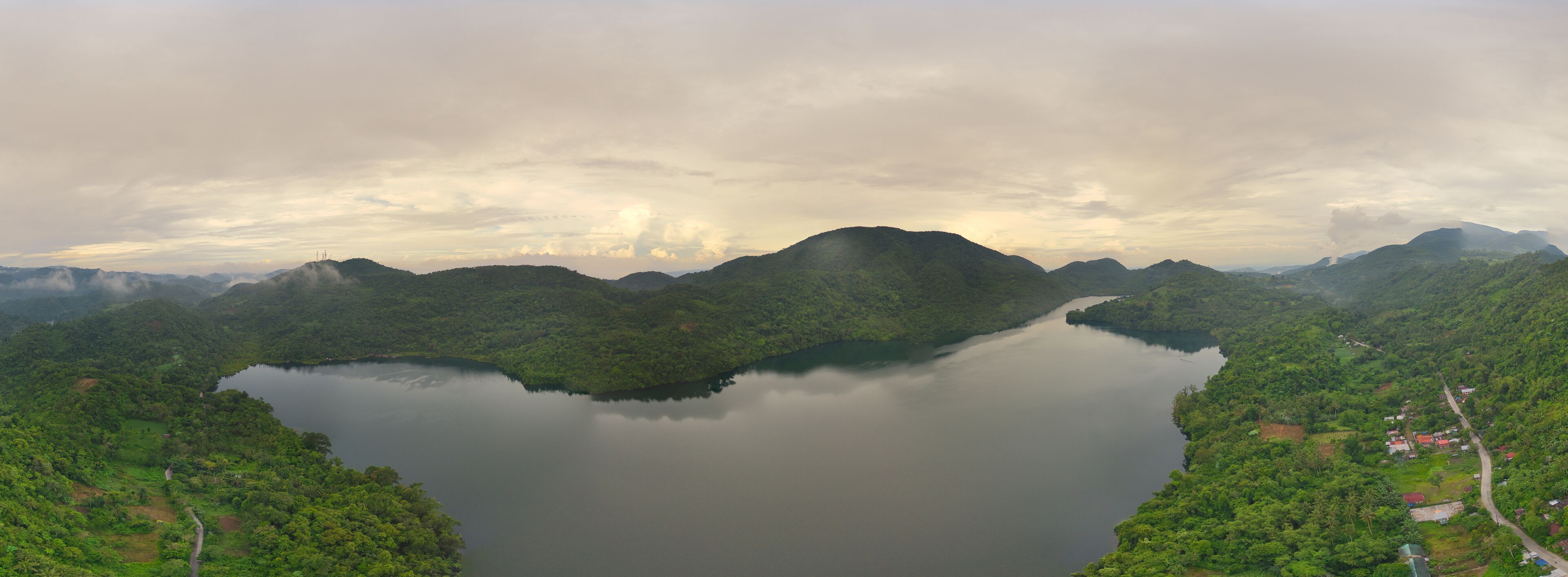 A lake surrounded by lush green hills and a cloudy sky.