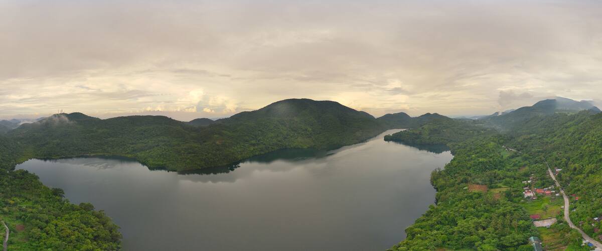 A lake surrounded by lush green hills and a cloudy sky.