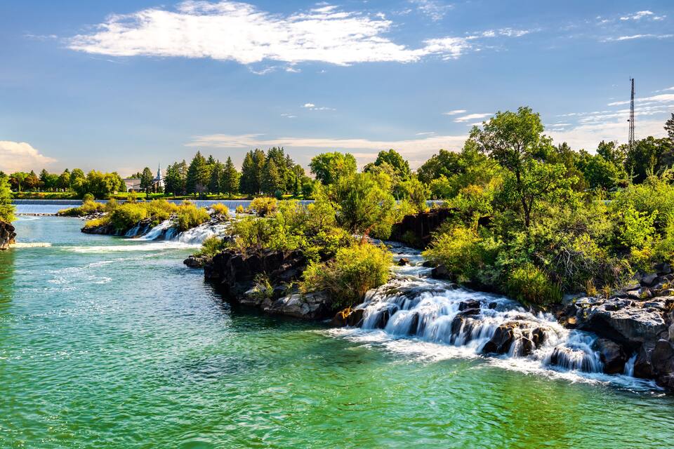 A river with multiple waterfalls surrounded by lush greenery and trees.
