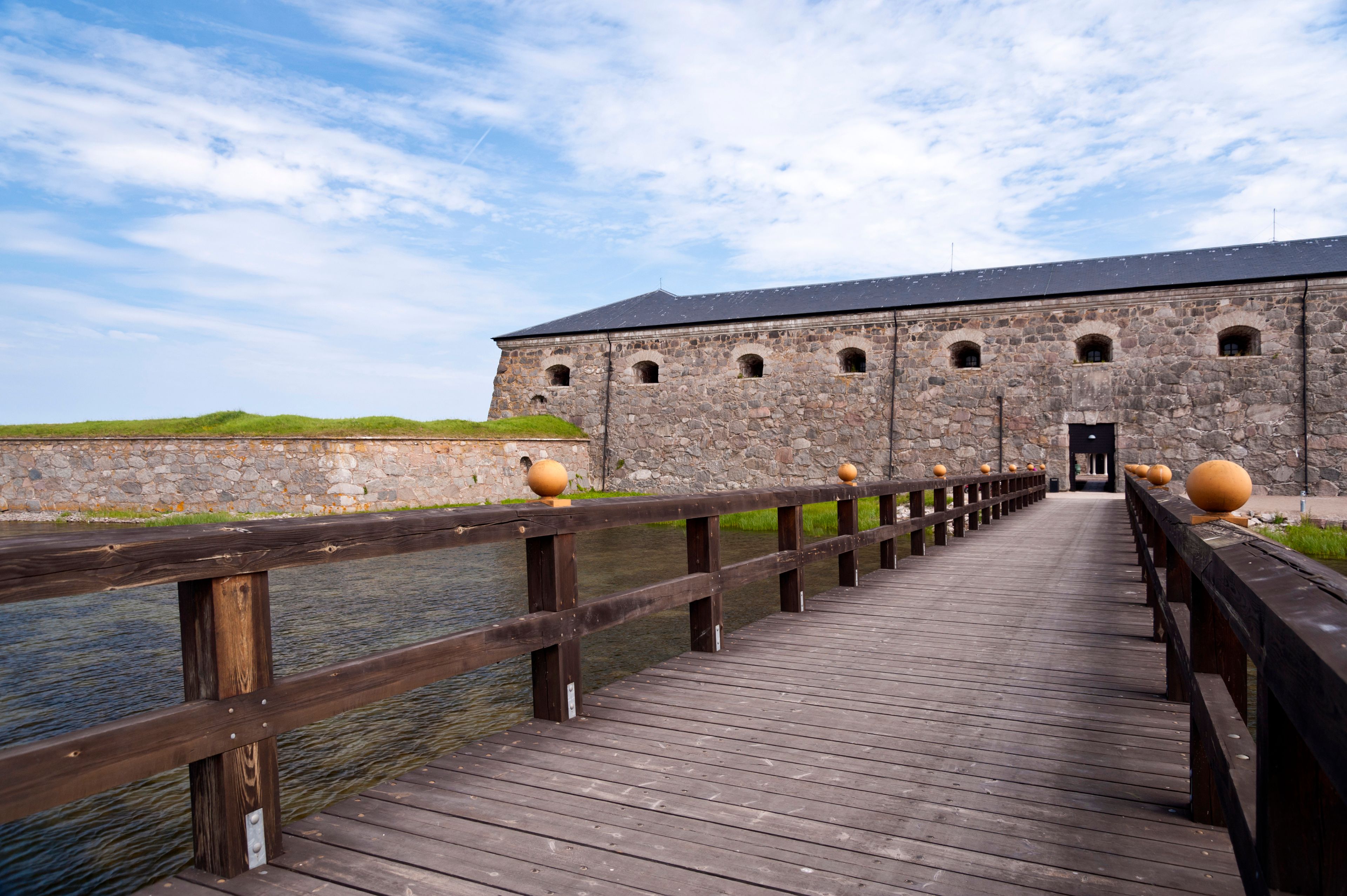 A wooden bridge leading to a stone fortress with arched windows.