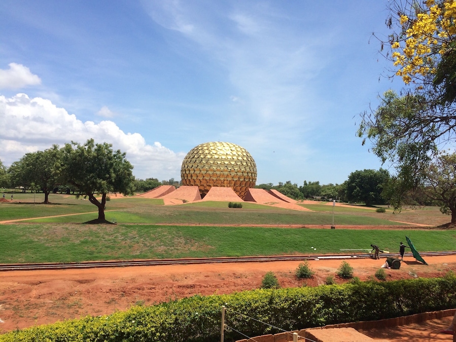 Una gran esfera dorada en un parque con césped verde, árboles y cielo despejado.
