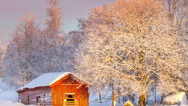 A wooden cabin in a snowy landscape with frosty trees.