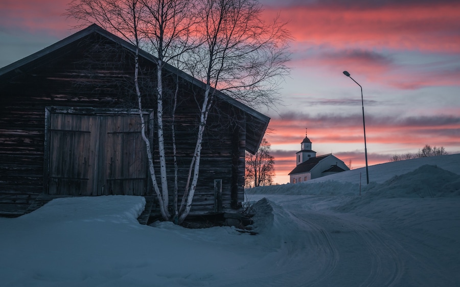 Sweden Jämtland (Lapland). The church of Storsjö, a cozy town next to Ljungdalen during blue hour. An old barn in the foreground. Snow is melting.