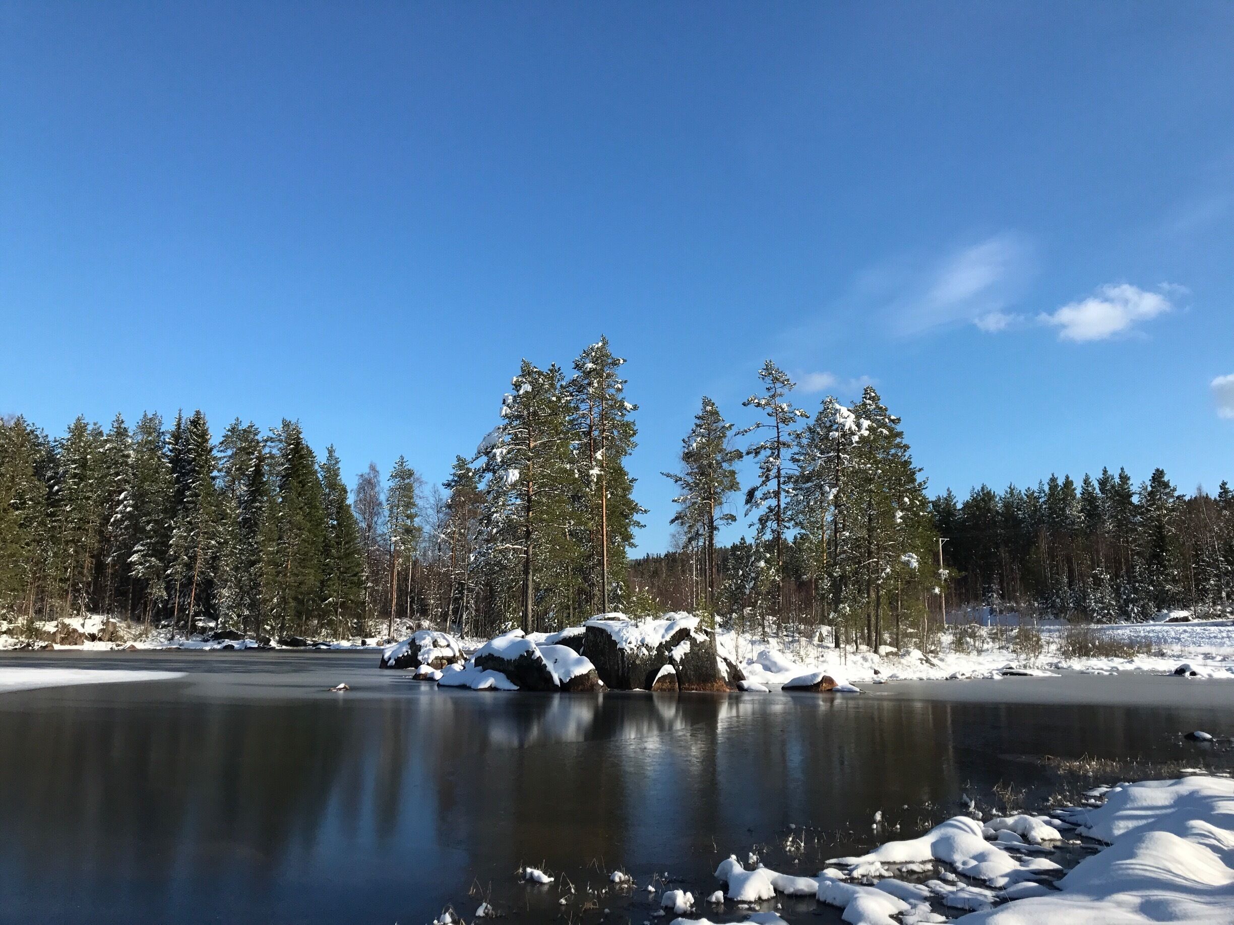 A frozen lake surrounded by snow-covered trees and rocks.