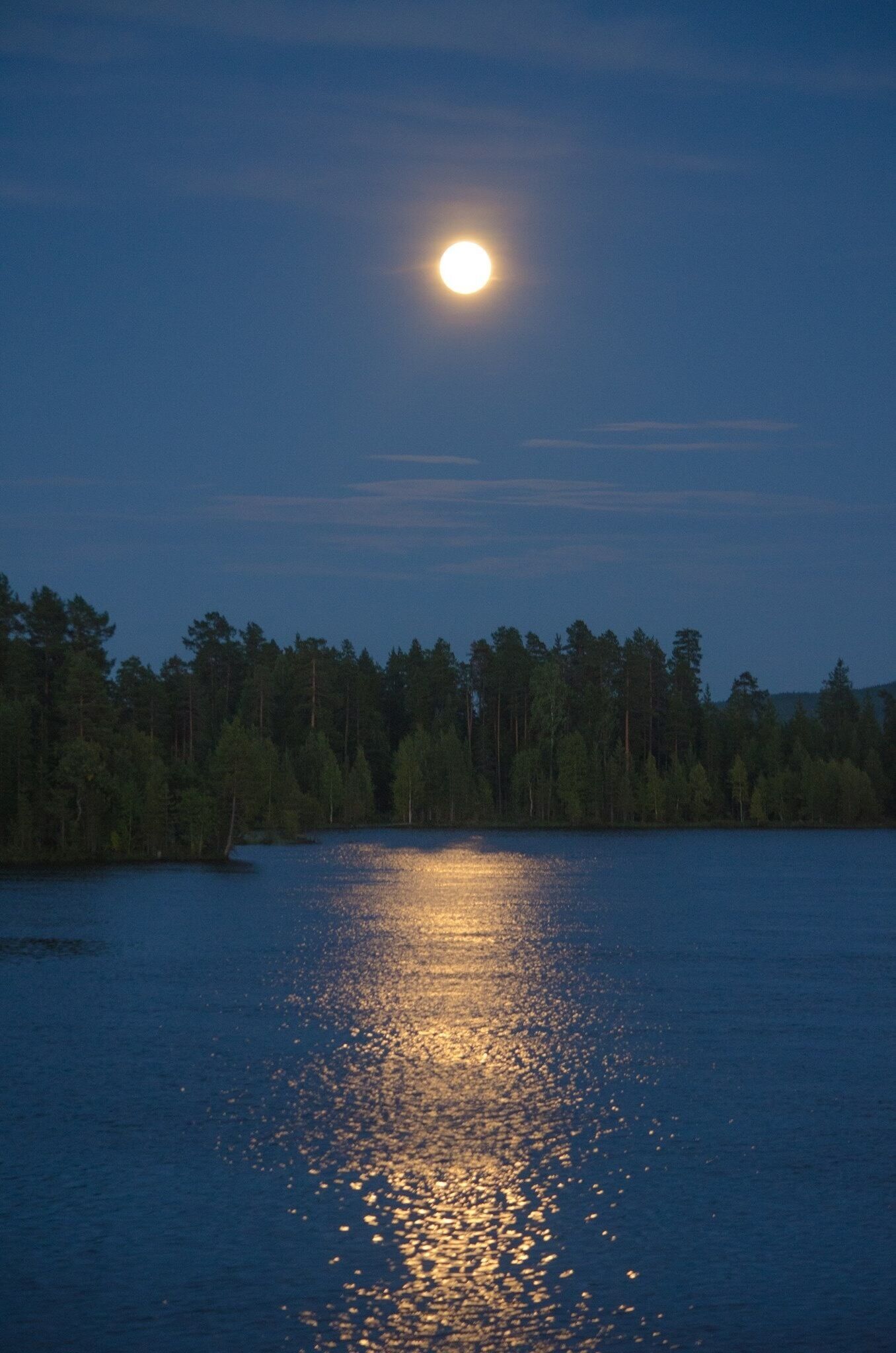 A lake at dusk with a full moon reflecting on the water's surface.