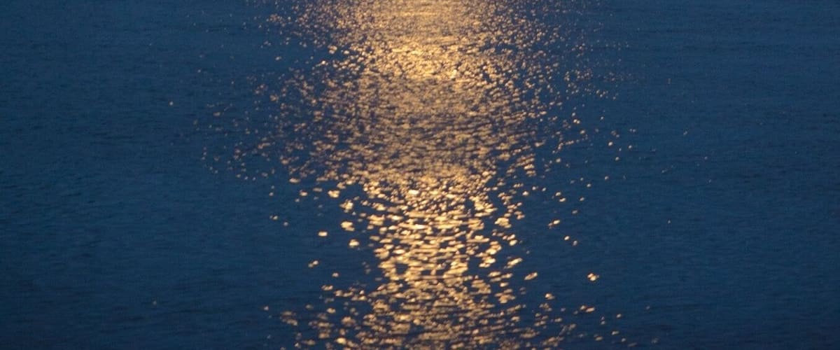 A lake at dusk with a full moon reflecting on the water's surface.