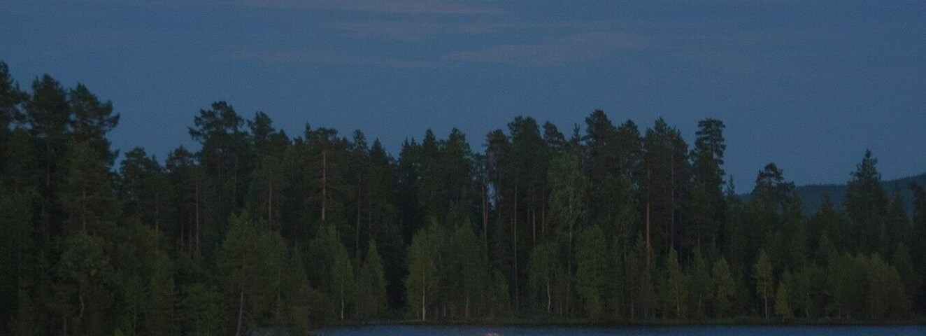 A lake at dusk with a full moon reflecting on the water's surface.