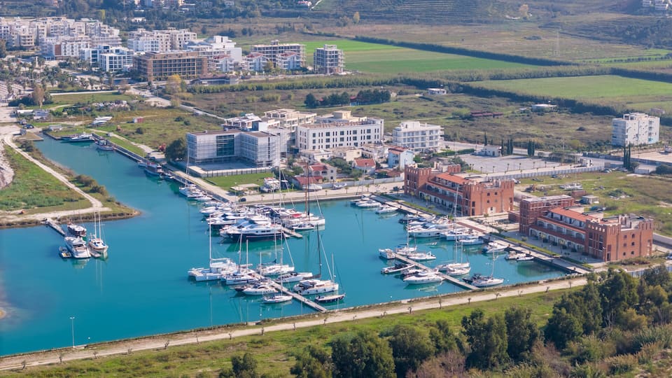A marina with boats docked, surrounded by buildings and greenery.