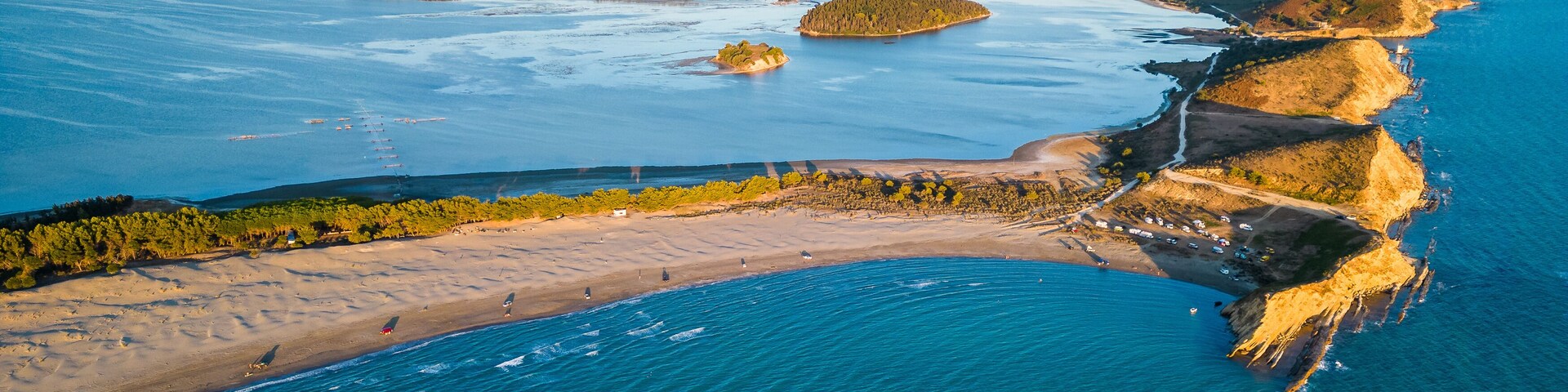 An aerial view of a coastal area with a sandy beach, a rocky coastline, and several small islands.