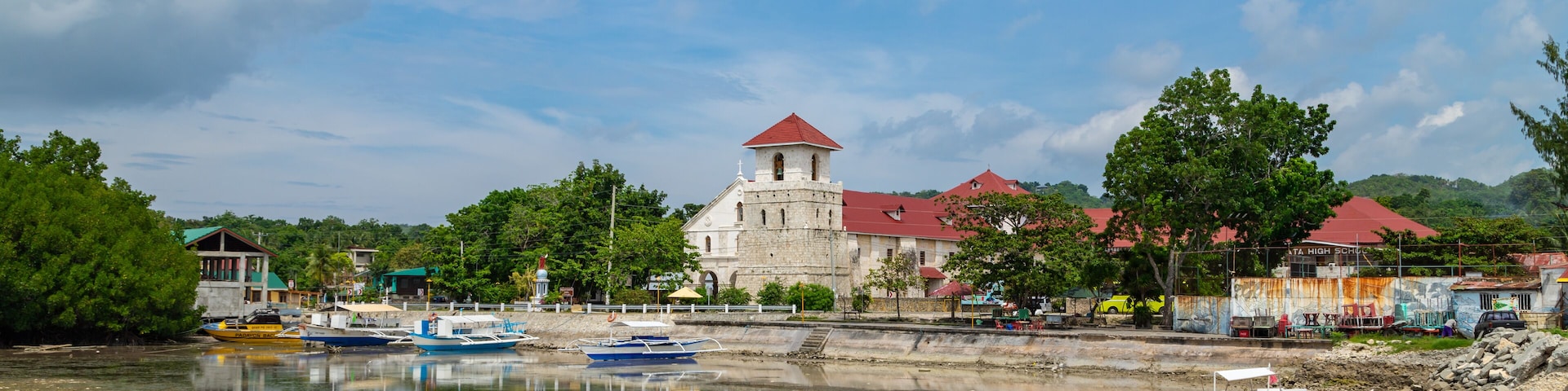 A river with boats, a church with a red roof, and surrounding greenery.