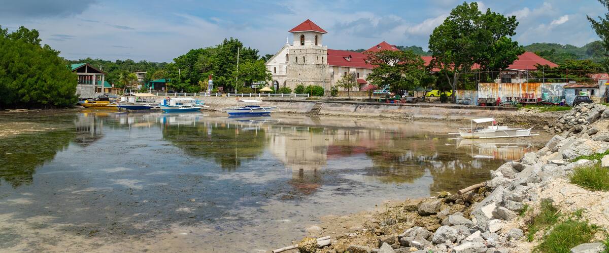A river with boats, a church with a red roof, and surrounding greenery.