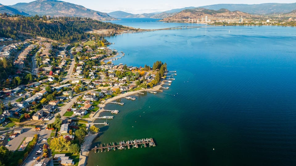 An aerial view of a coastal town with a marina, residential area, and surrounding hills.