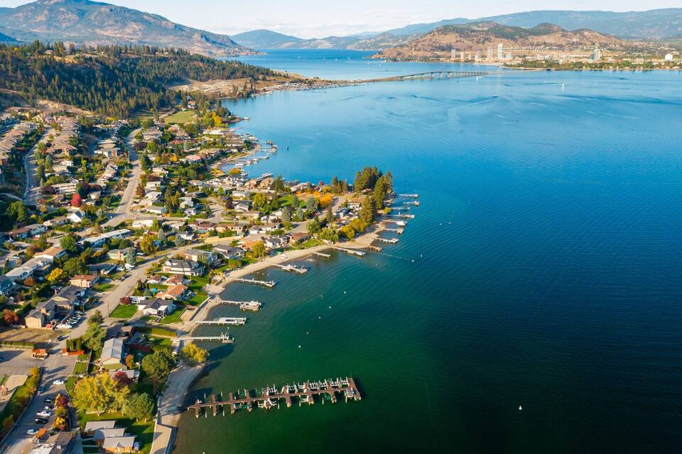 An aerial view of a coastal town with a marina, residential area, and surrounding hills.