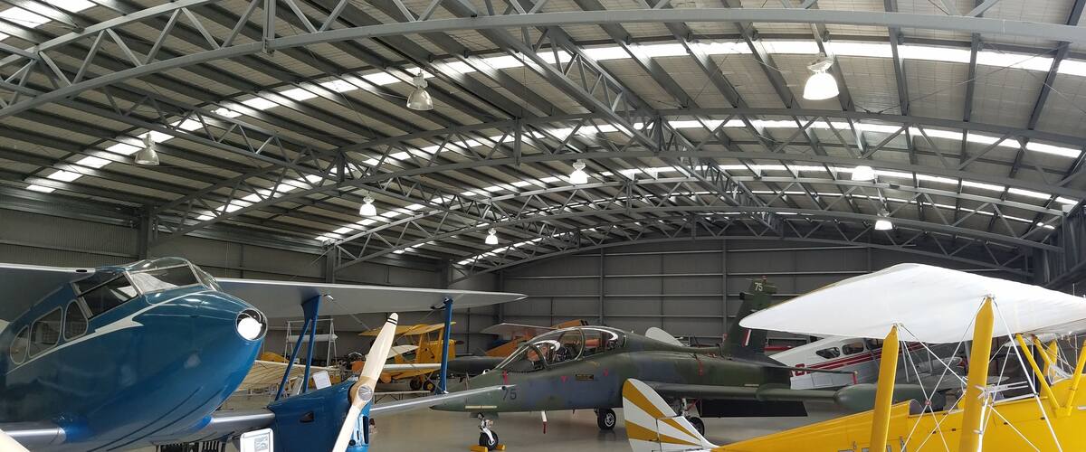 A hangar with various aircraft, including a blue plane and a yellow biplane.