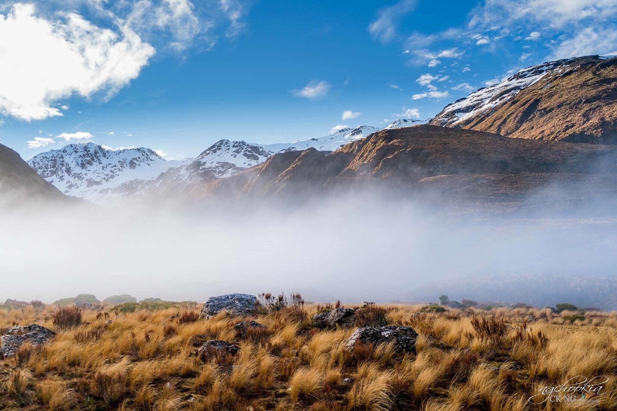 A mountainous landscape with snow-capped peaks, a grassy foreground, and a clear blue sky.