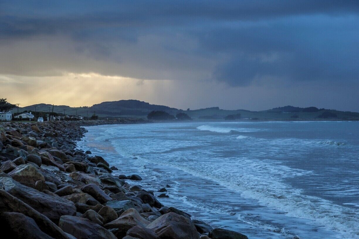A rocky coastline with waves crashing against the shore, under a cloudy sky.