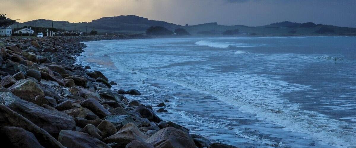A rocky coastline with waves crashing against the shore, under a cloudy sky.