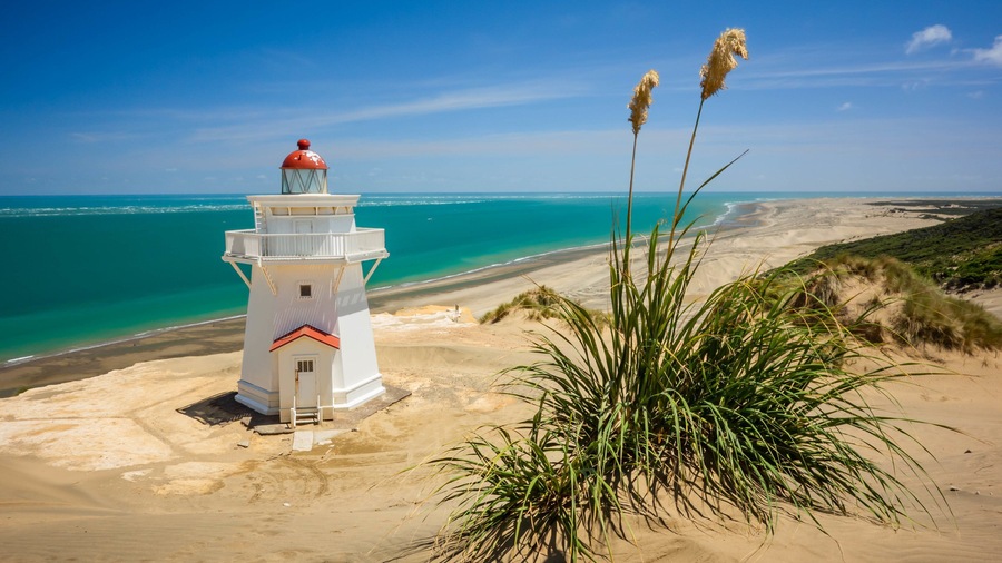 Un faro blanco con parte superior roja sobre una playa arenosa y agua azul cristalina.