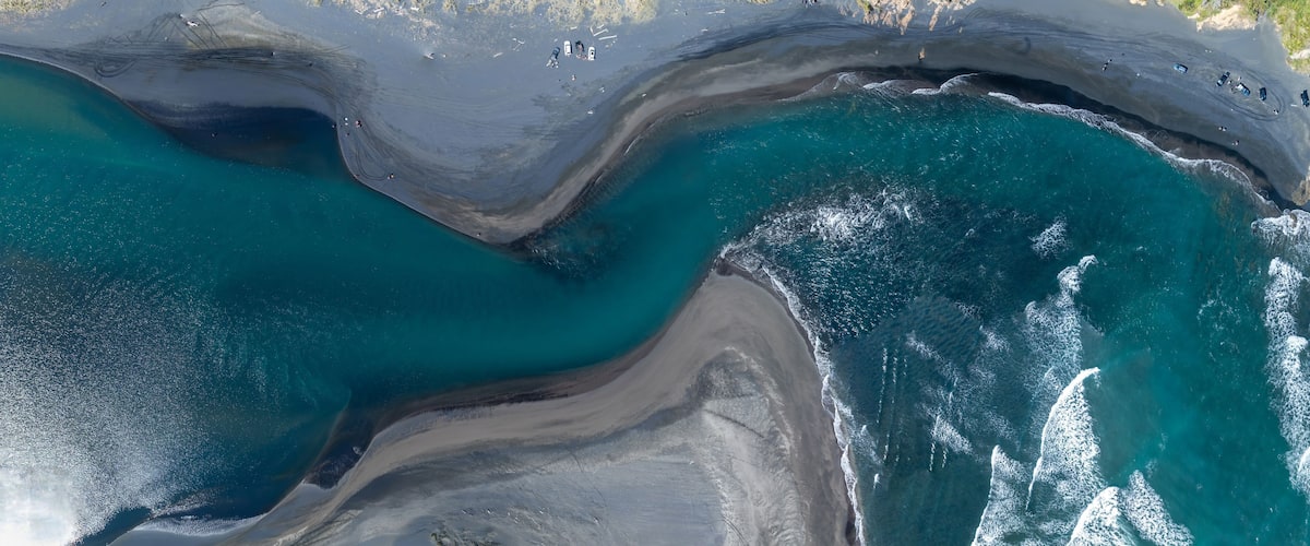 An aerial view of a beach with clear turquoise waters, a sandy shoreline, and a few scattered boats.