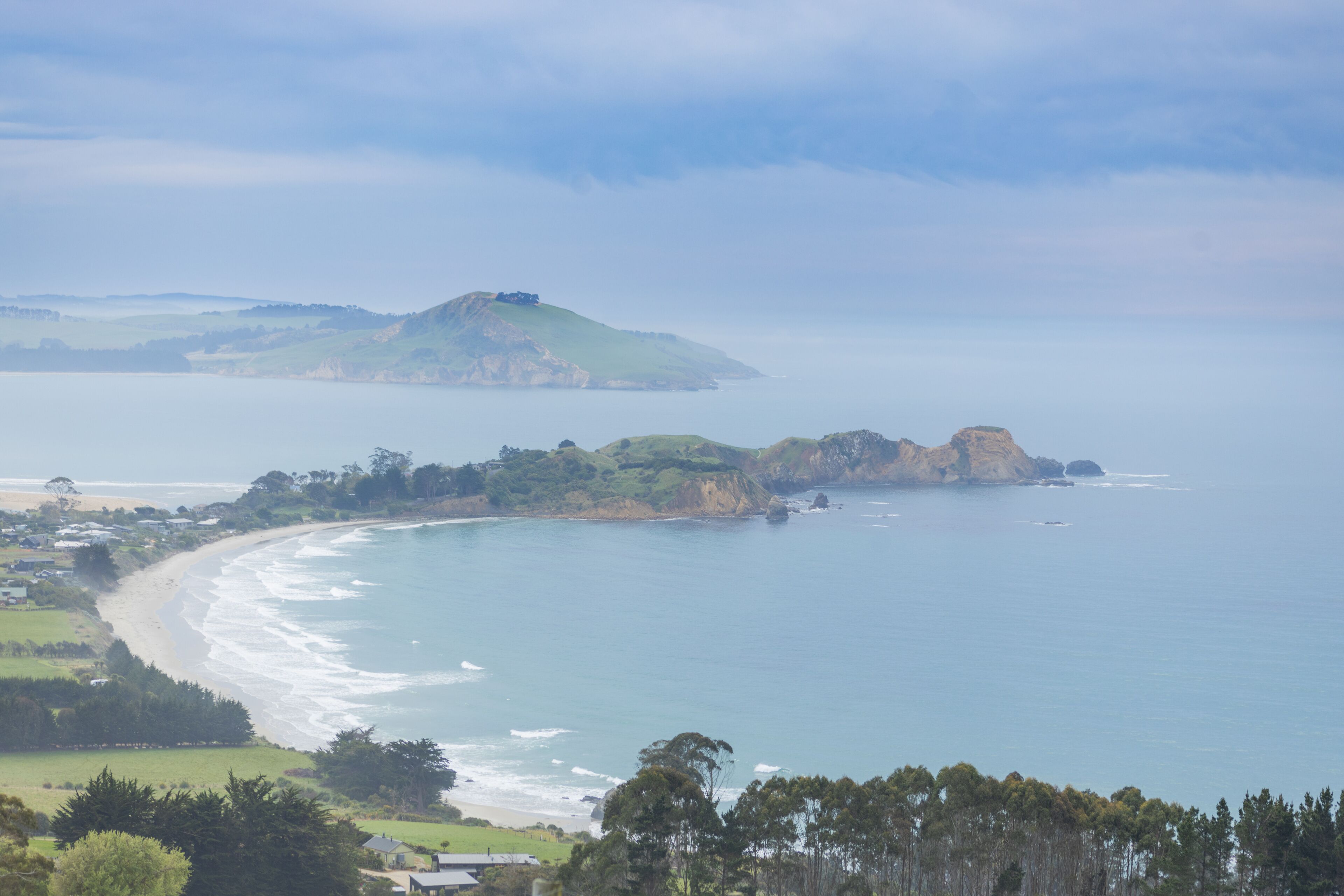 A coastal landscape with a beach, cliffs, and a distant mountain.