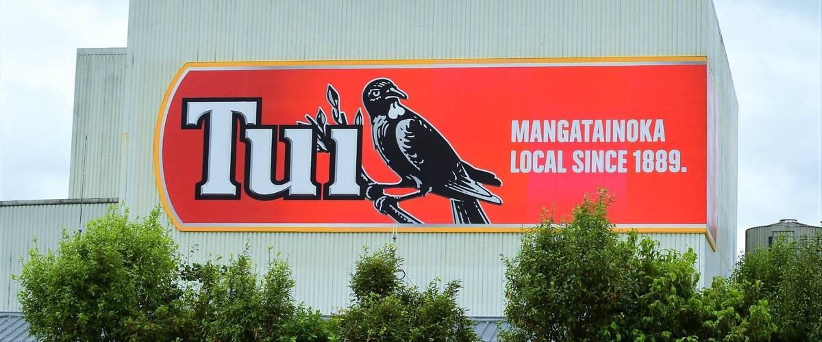 A large billboard with a red background and a black bird illustration, featuring the word 'Tui' and the text 'Mangatainoa Local since 1889.'