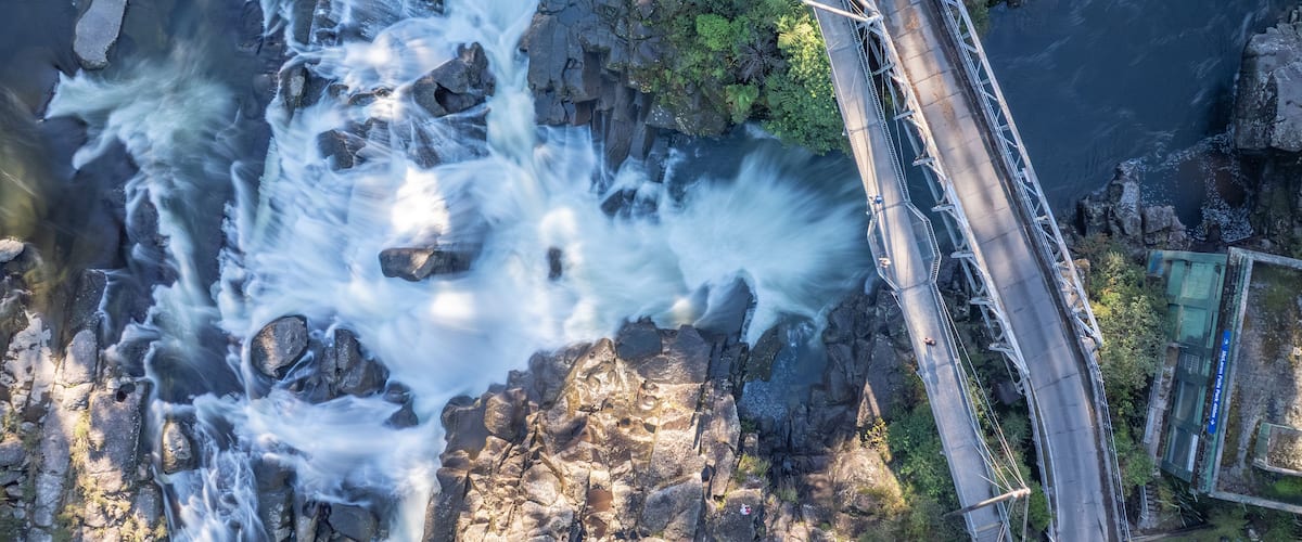 A waterfall cascading over rocks, a bridge, and a road with vehicles.