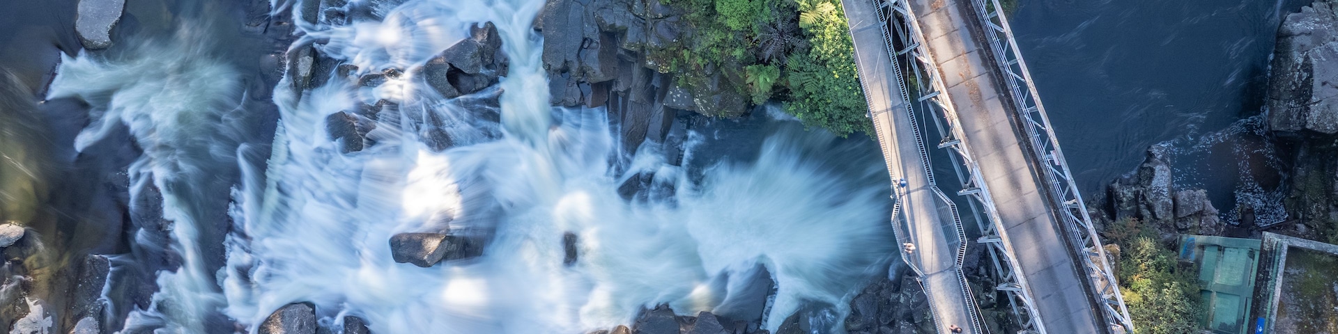 Una cascada que cae sobre rocas, un puente y una carretera con vehículos.
