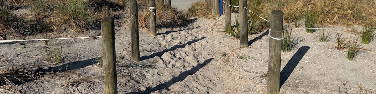Une plage de sable avec des poteaux en bois et une clôture faite de cordes qui mène à l’océan.