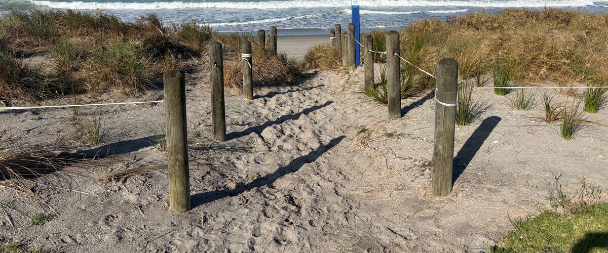 Una spiaggia sabbiosa con pali di legno e una recinzione di corde che conduce verso l'oceano.