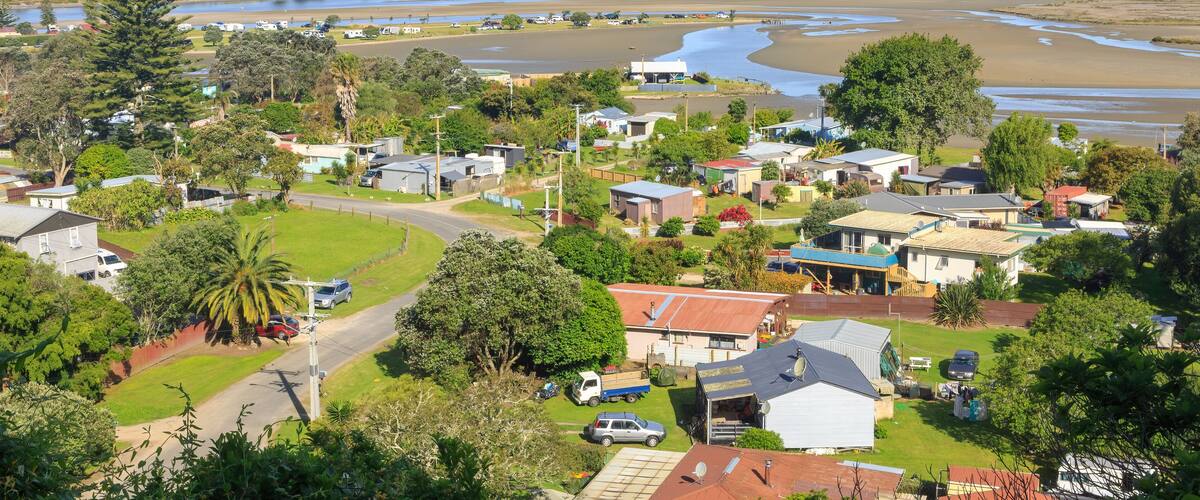 A coastal town with houses, a river, and a mountain range in the distance.